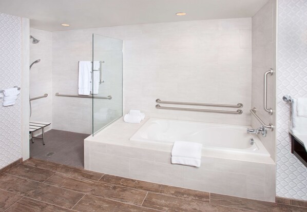 A modern bathroom with a large bathtub, glass shower enclosure, and handrails.