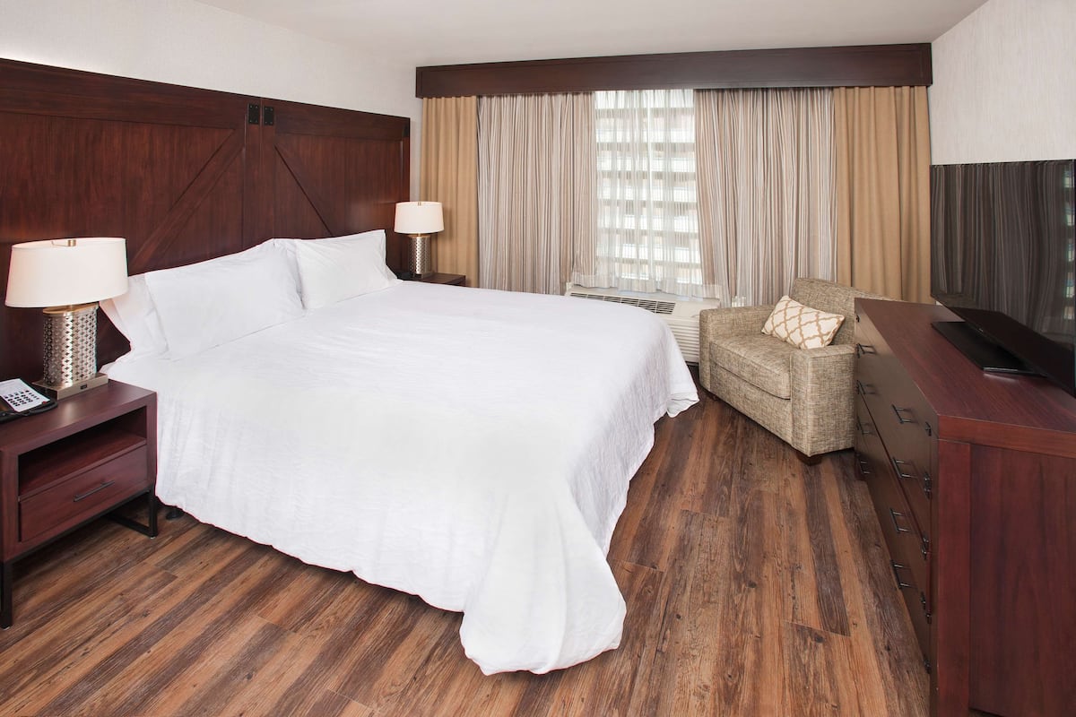 Habitación de hotel con una cama grande, un televisor, una silla y un escritorio con lámpara.
