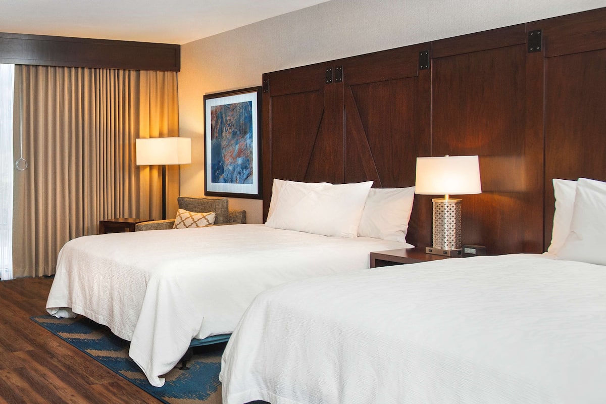 Habitación de hotel con dos camas, un cuadro grande en la pared, una ventana con cortinas y un calentador en el suelo.