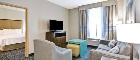 A hotel room with a bed, a television, a sofa, a chair, a small table, and a lamp.