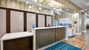 A hotel reception area with a reception desk, a blue carpet with "Homewood Suites by Hilton" text, and a decorative ceiling with lights.