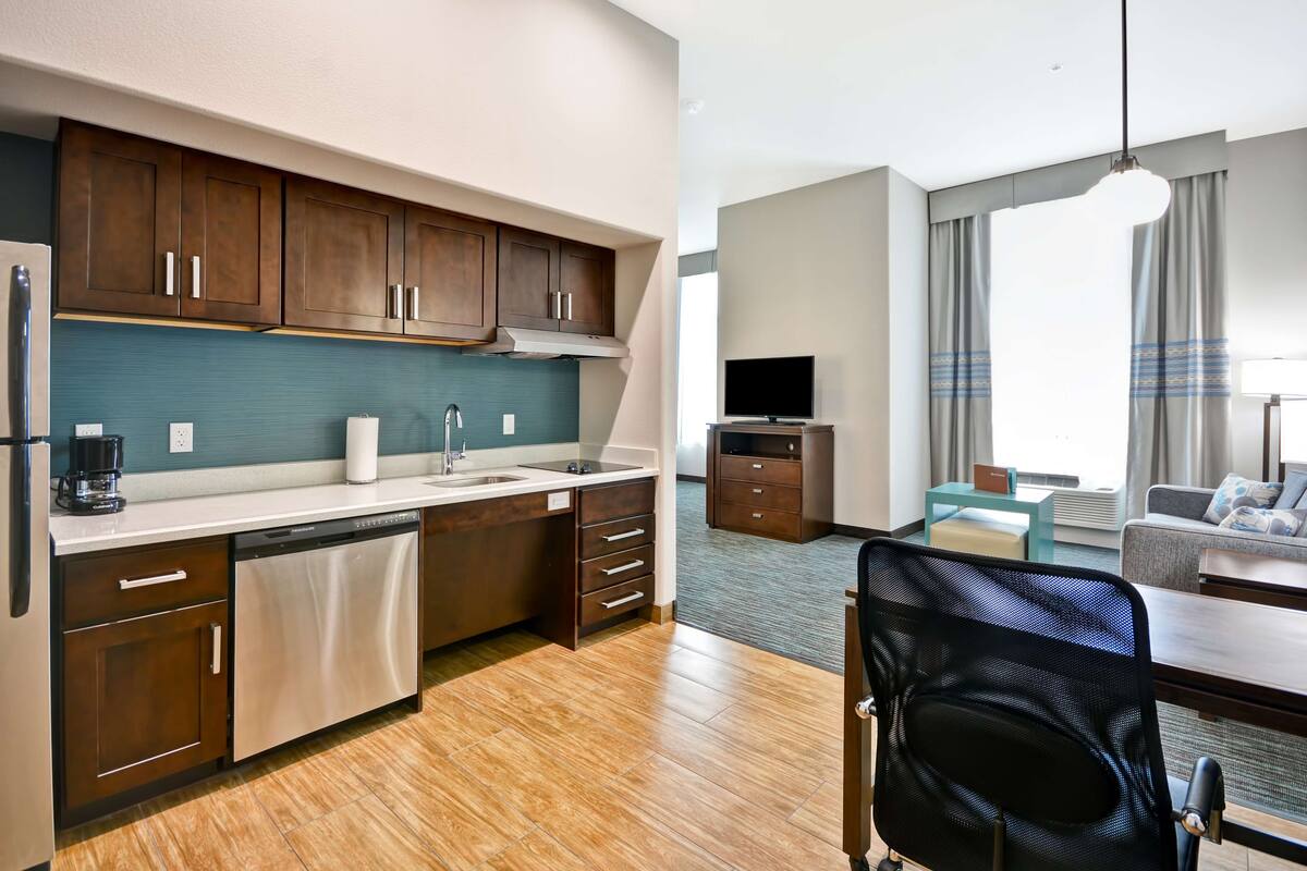 A compact hotel room with a kitchenette, a sofa, a TV, and a dining area.