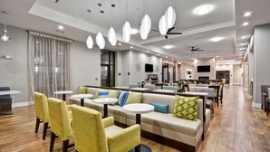Un moderno vestíbulo de hotel con zonas de estar, una cocina al fondo y un ventilador de techo.