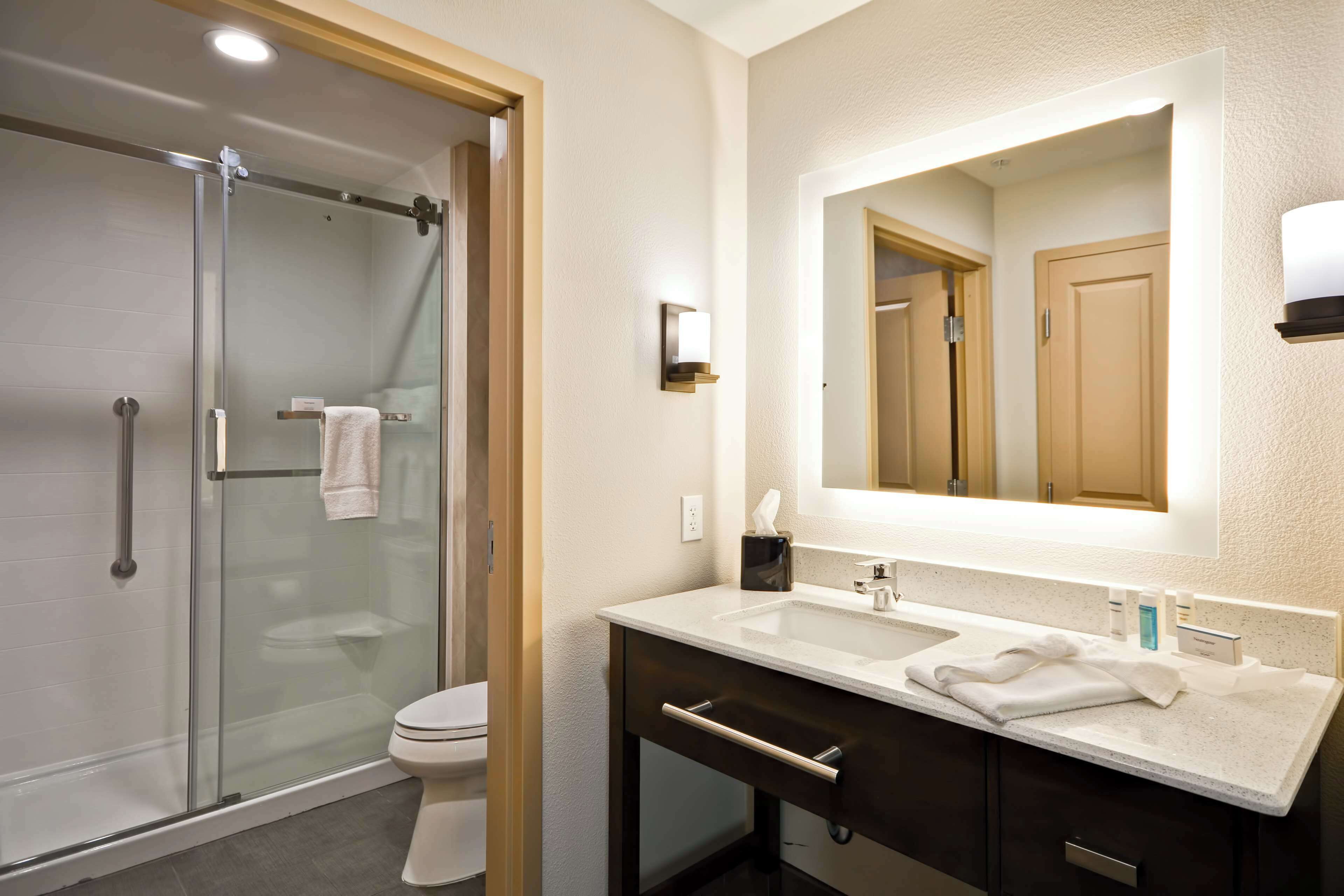 A modern bathroom with a glass shower enclosure, a white toilet, a vanity with a mirror, and a countertop with toiletries.