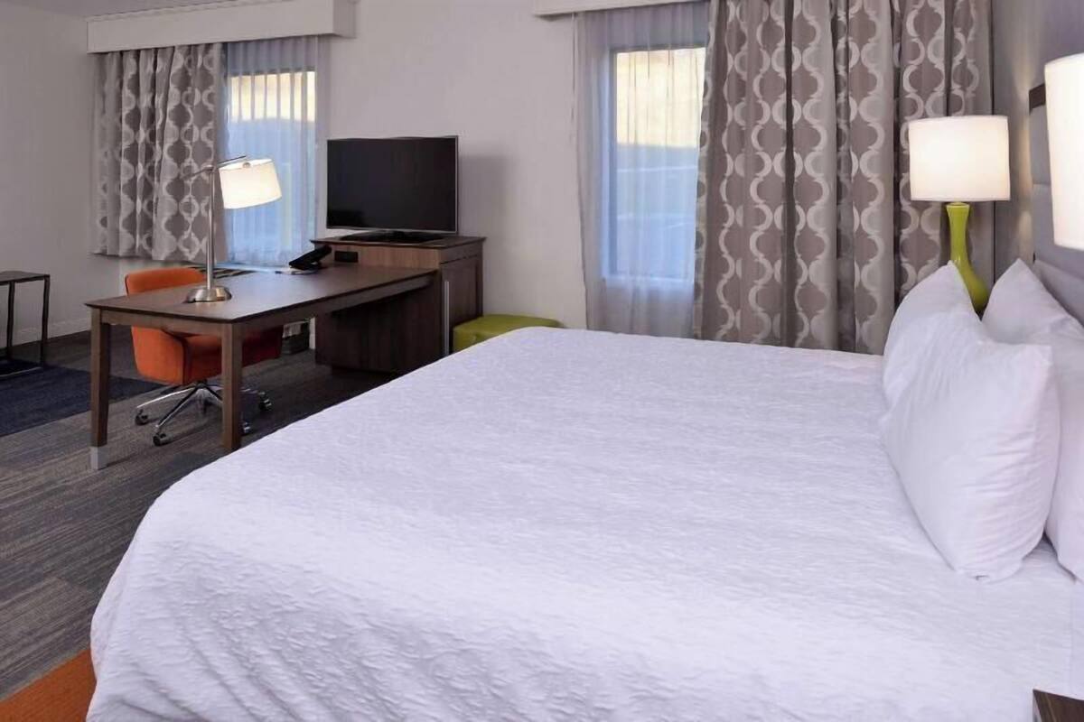 Hotellihuone, jossa on suuri sänky, työpöytä tuolilla, televisio ja kaksi lamppua.