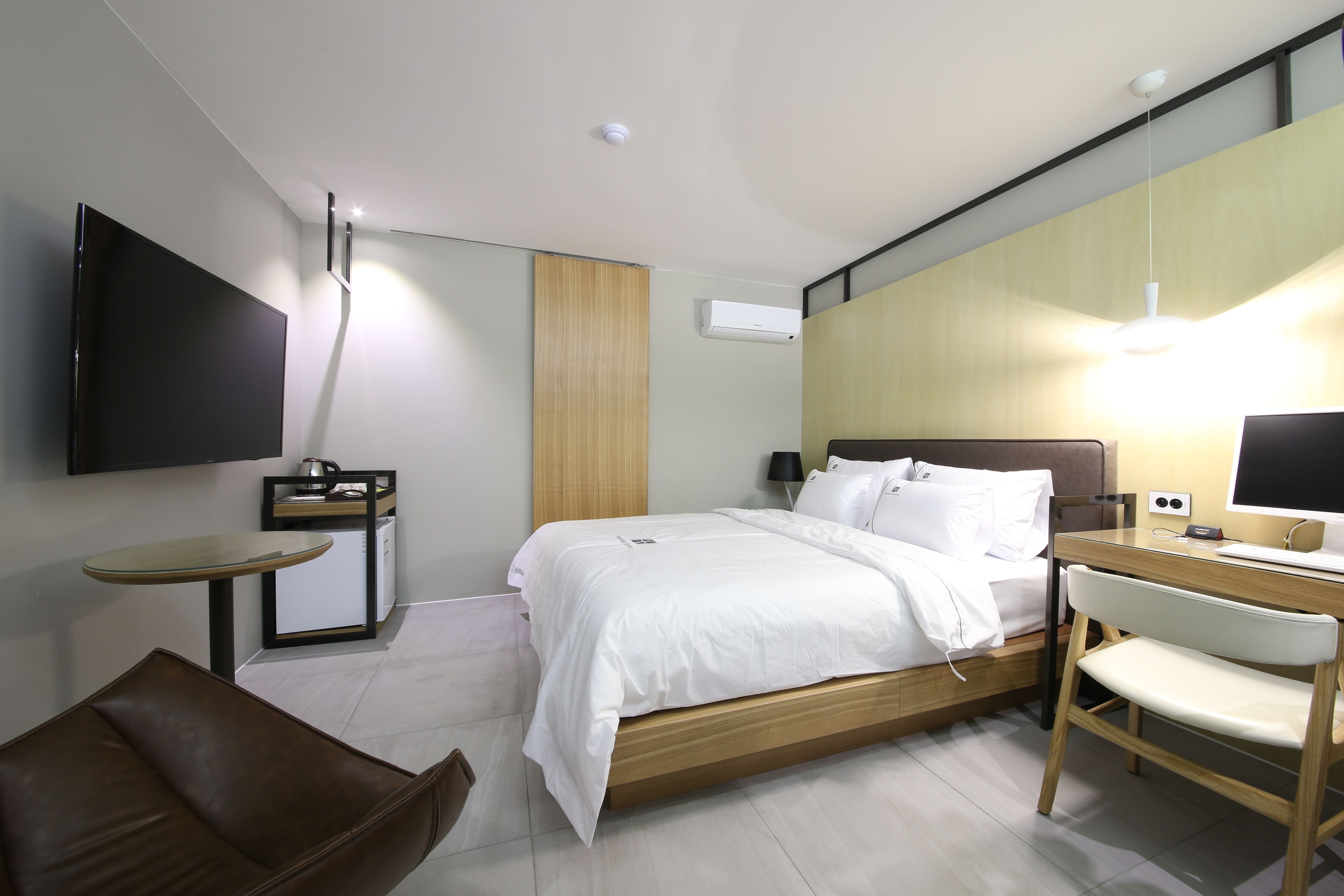 A modern hotel room with a bed, a desk, a chair, a TV, and an air conditioning unit.