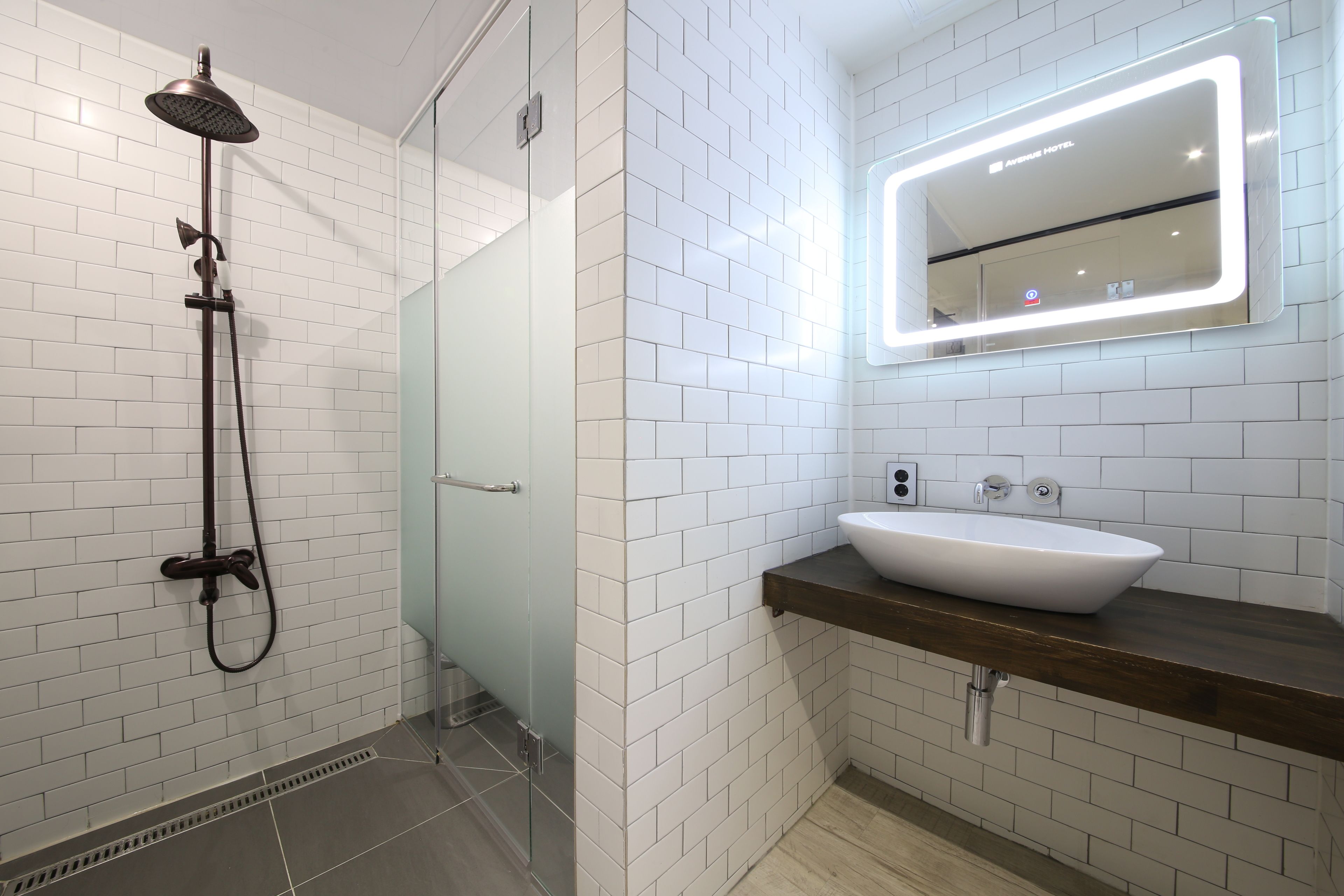 A modern bathroom with white subway tiles, a glass shower enclosure, a white sink with a wooden countertop, and a mirror with integrated lighting.
