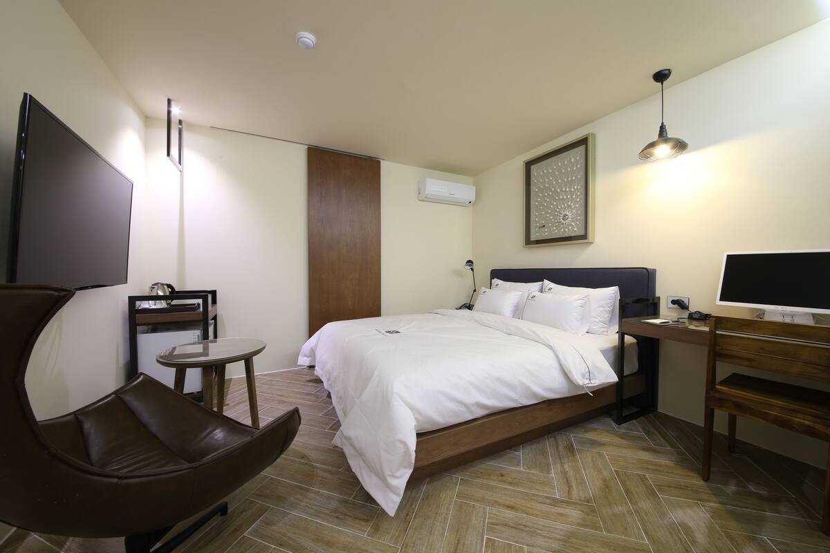 A modern hotel room with a large bed, a desk, a chair, and a flat-screen TV.