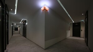 A modern hallway with a geometric light fixture on the wall, a clean floor, and a door at the end. - Avenue Hotel (Jeonju)