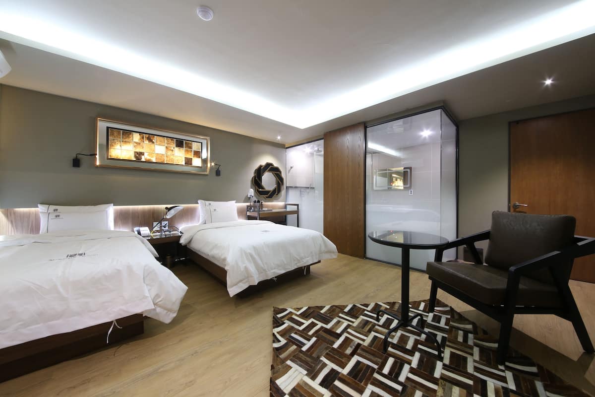A hotel room with two beds, a desk, a chair, and a large mirror.
