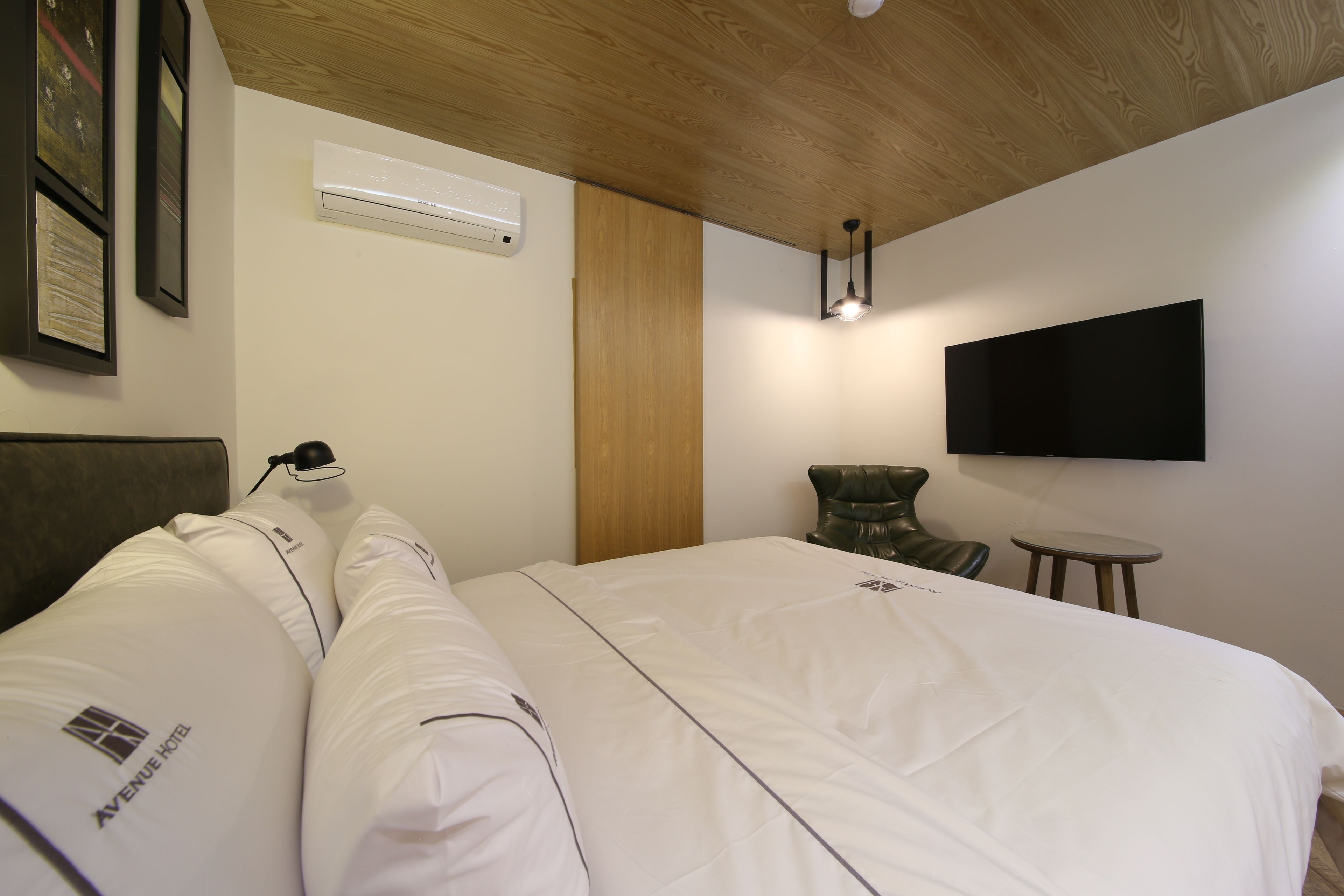 Habitación de hotel con una cama grande, un televisor de pantalla plana montado en la pared, techo de madera y un equipo de aire acondicionado.