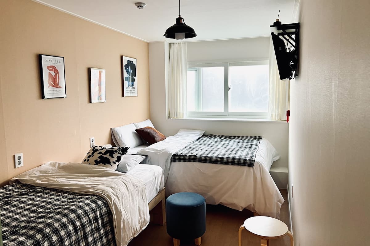 A bedroom with two beds, a window, and artwork on the wall.