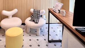 A modern room with two plush, animal-shaped chairs, a small yellow ottoman, and a wooden desk with a computer and a menu. - ARA125 (Seoul)