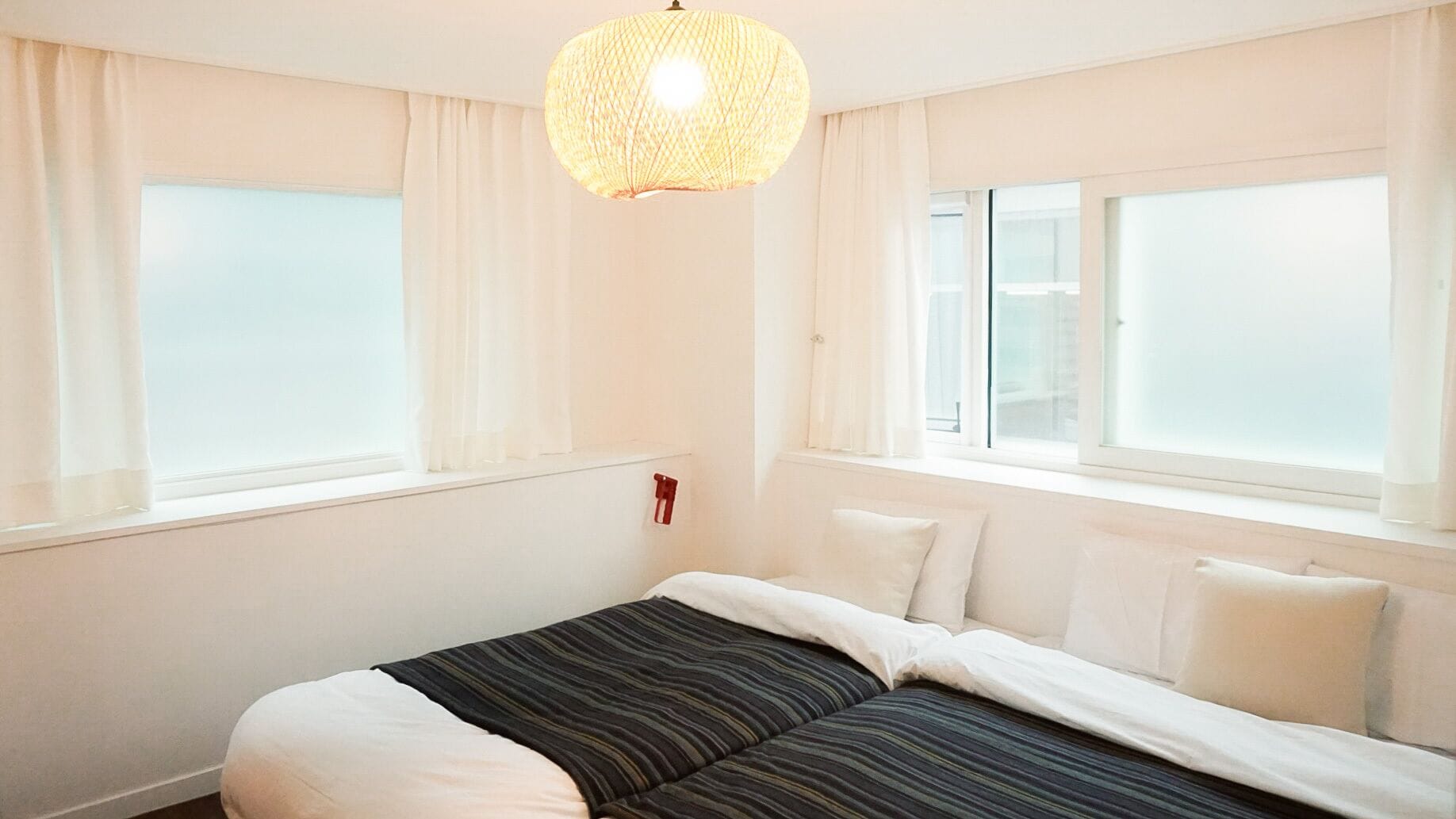 A hotel room with a bed, two windows, and a hanging light fixture.