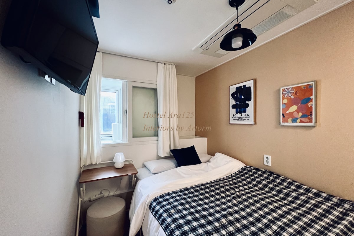 A hotel room with a bed, a desk, a chair, a TV, and artwork on the wall.