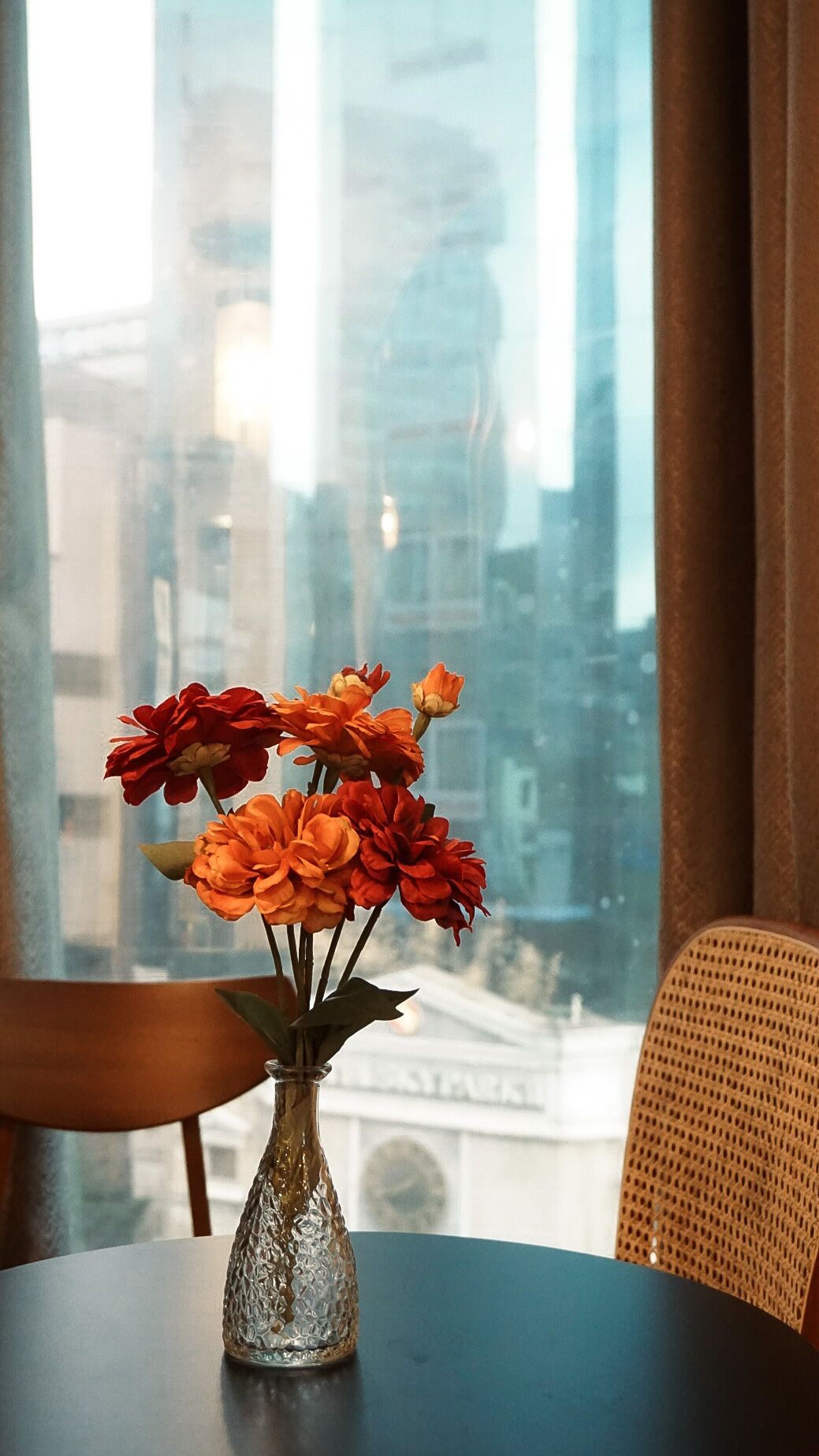 A vase with flowers on a table by a window with a cityscape view.