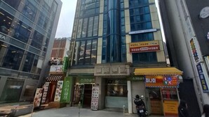 A modern building with a glass facade, a prominent cylindrical structure, and a sign for a hotel named "HOTEL Avia". - ARA125 (Seoul)