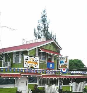 A building with a green facade, a red roof, and multiple signs including "Cocopele Inn" and "L. Gukory". - Cocopele Inn (San Ignacio)