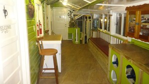 A narrow hallway with a wooden chair and a small table, a door with a 'WELCOME' sign, and a green wall with a water dispenser. - Cocopele Inn (San Ignacio)
