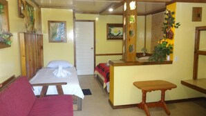 A room with a bed, a wooden bench, a sofa, a mirror, and a door. - Cocopele Inn (San Ignacio)