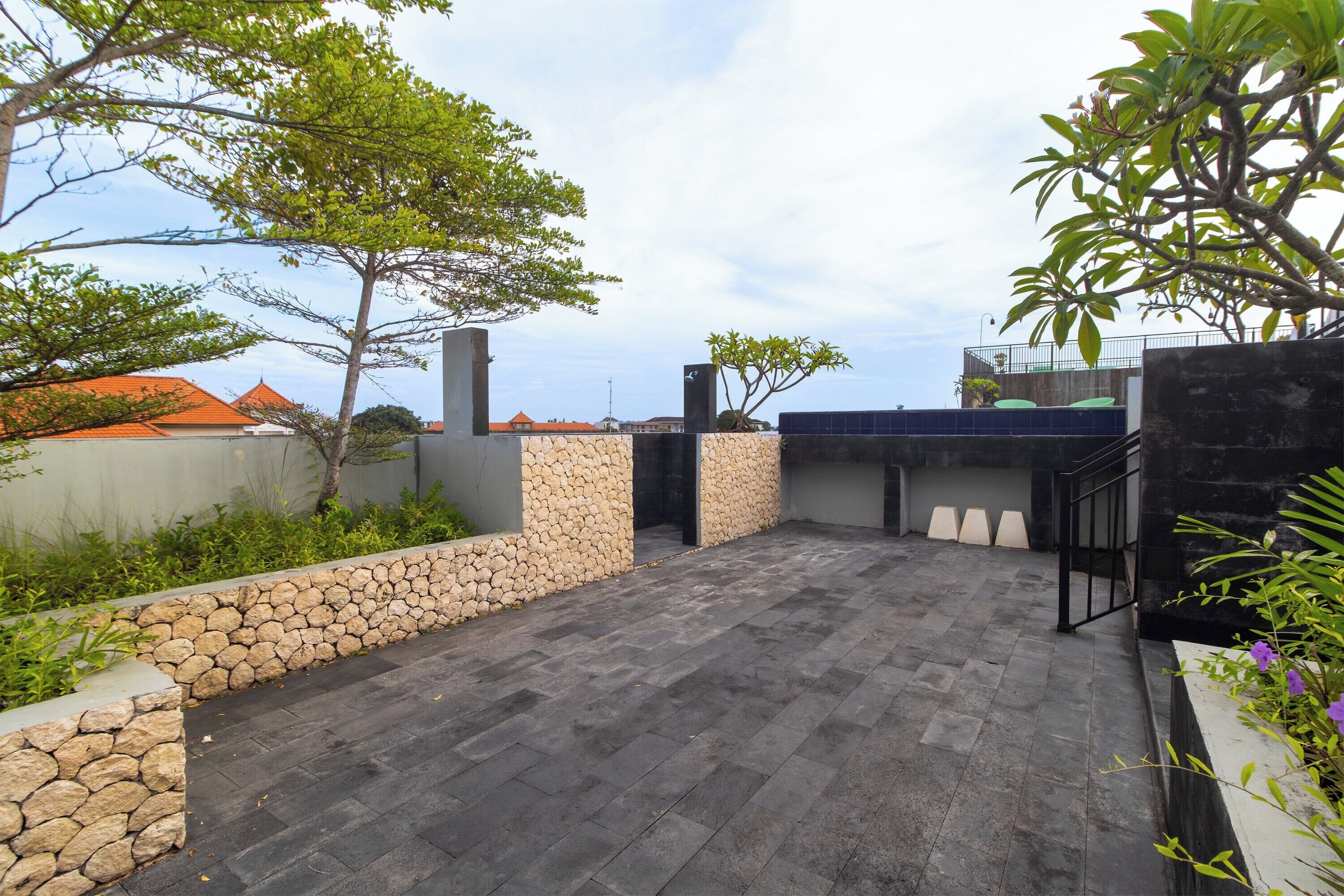 A paved outdoor area with stone walls, a metal railing, and greenery.