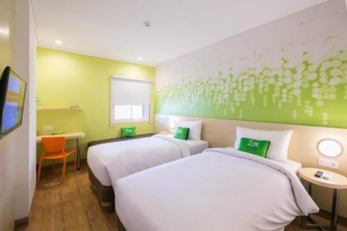 A hotel room with two beds, a desk, a chair, a small table, and a wall with a floral pattern.