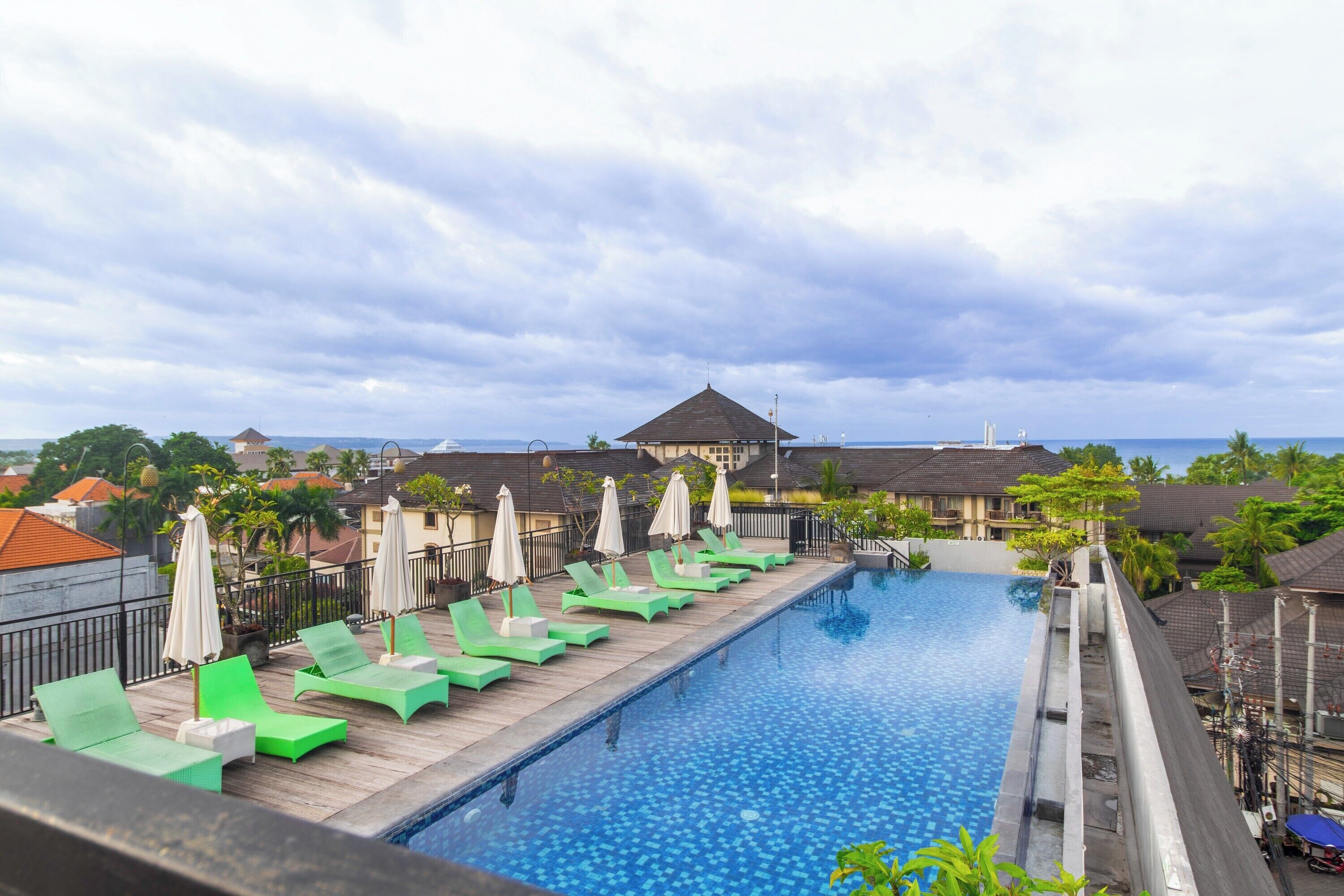 A swimming pool with lounge chairs and umbrellas, surrounded by buildings and a cloudy sky.