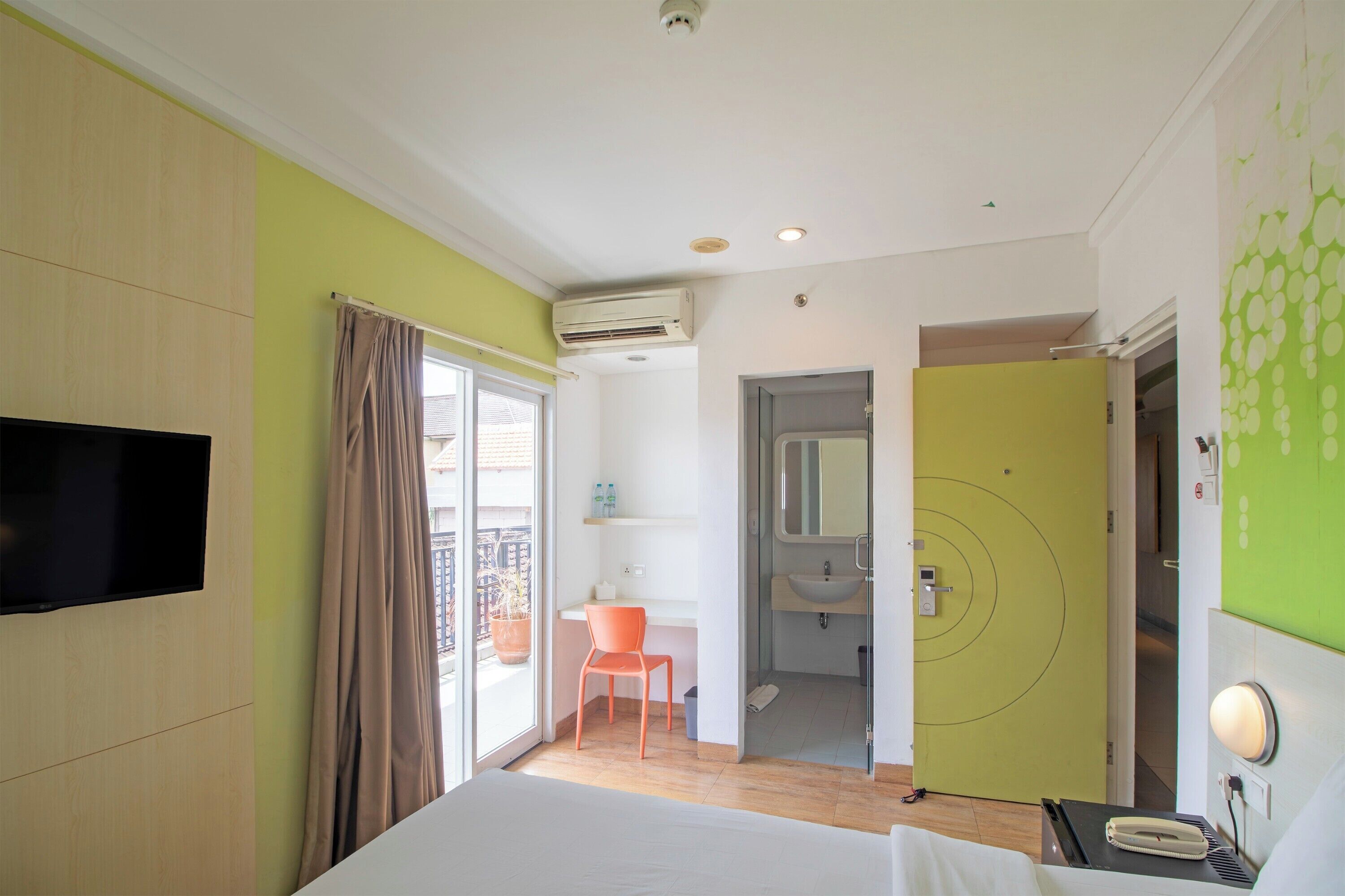 Een hotelkamer met een bed, een bureau, een stoel, een televisie, een badkamer en een balkon.