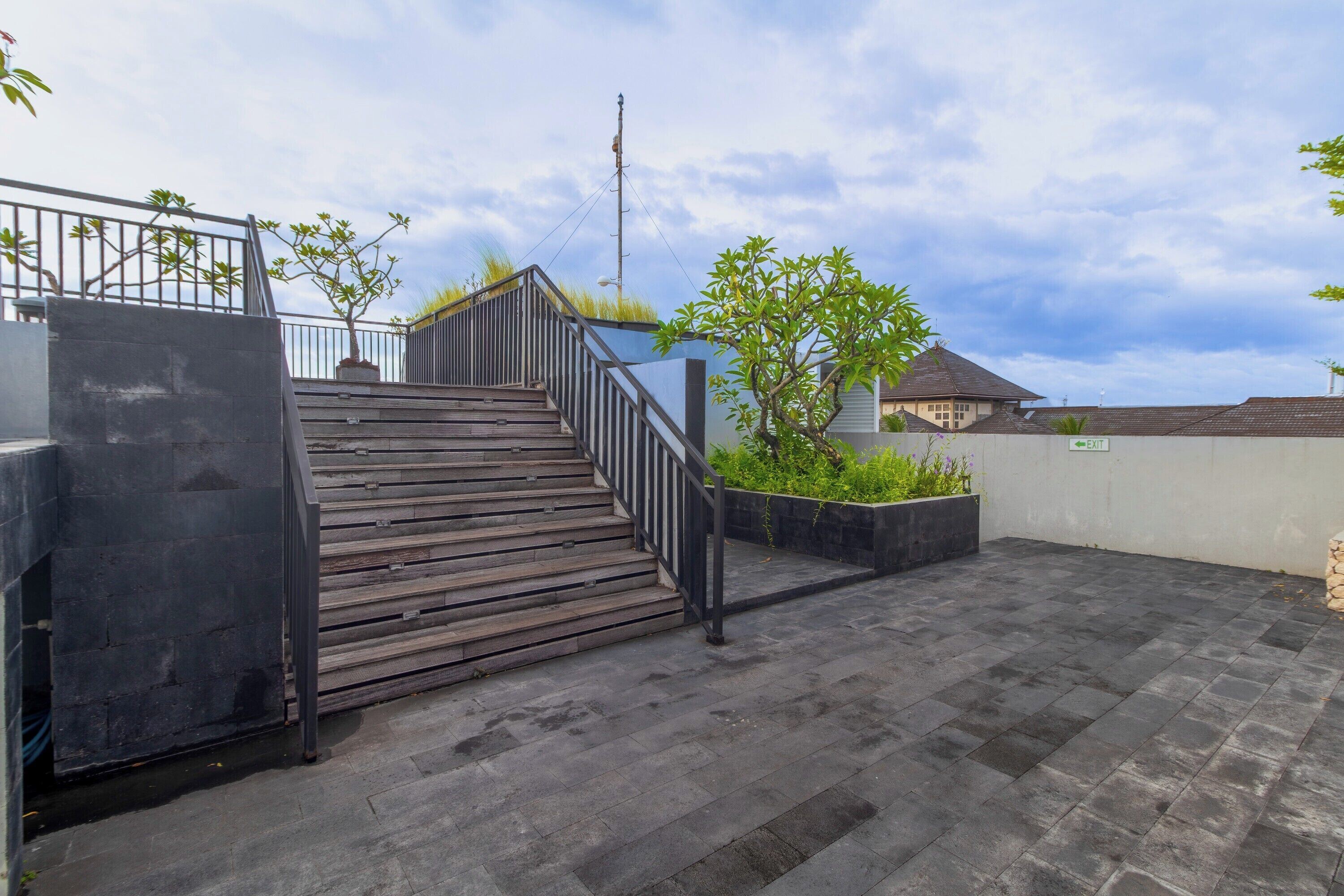 Une terrasse sur le toit, avec un escalier en bois, une rambarde en métal et une vue sur un immeuble en arrière-plan.