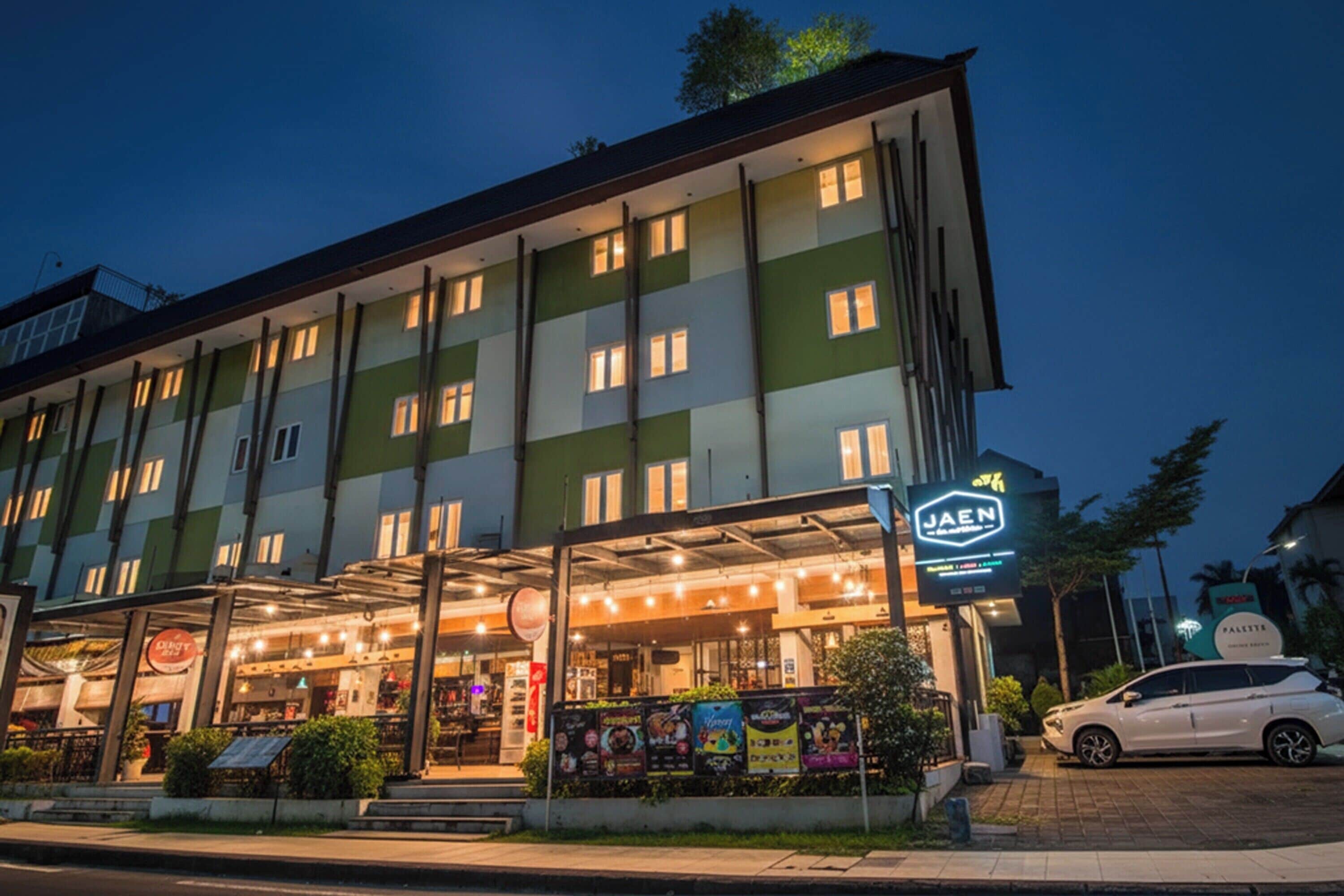 A multi-story hotel with a covered entrance, illuminated signage, and a parked car.