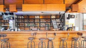 A bar area with wooden bar counter, metal stools, and shelves with bottles. - Palette Legian Beach (Legian)