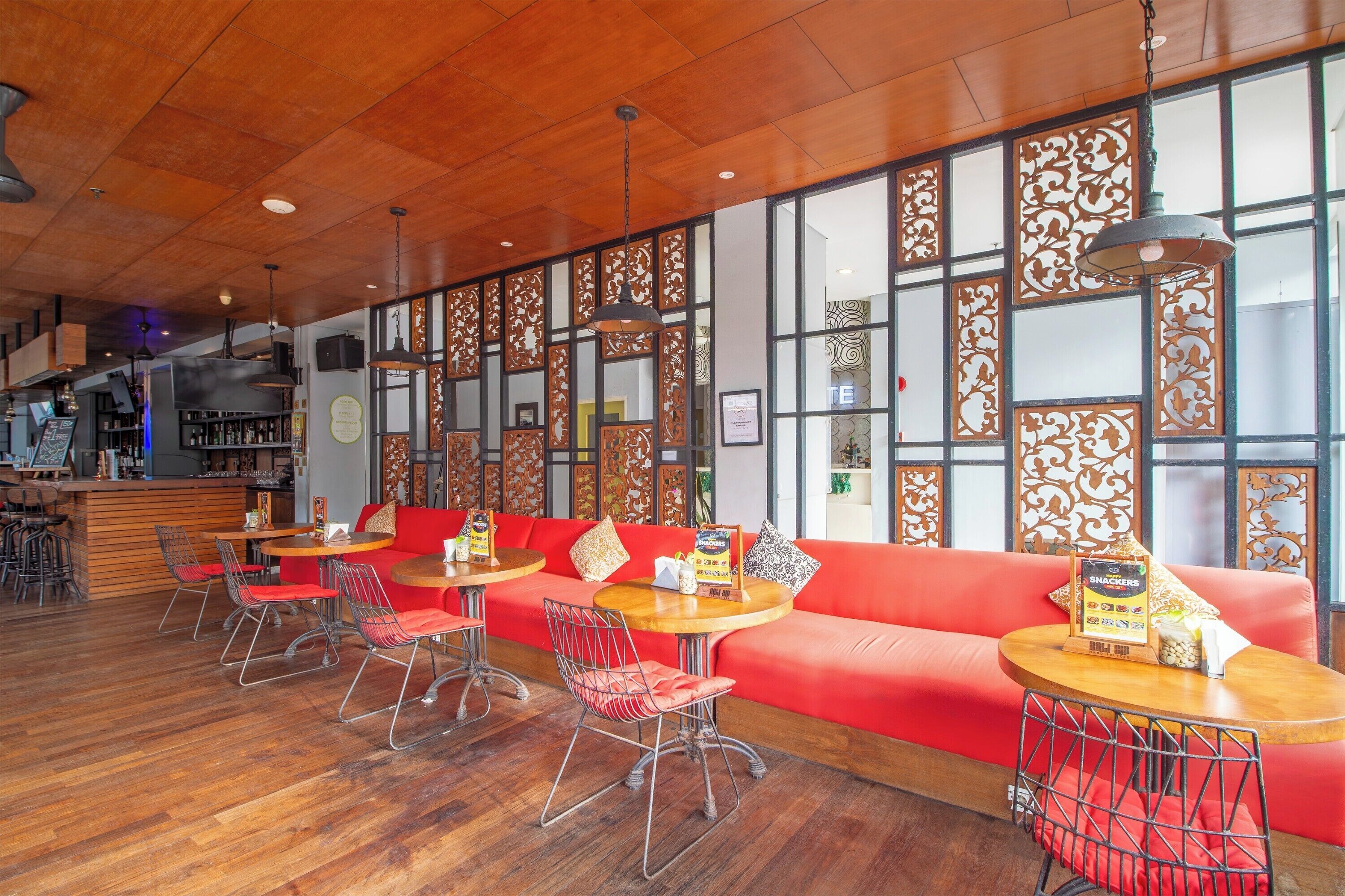 A restaurant with wooden flooring, red upholstered seating, and a bar area in the background.