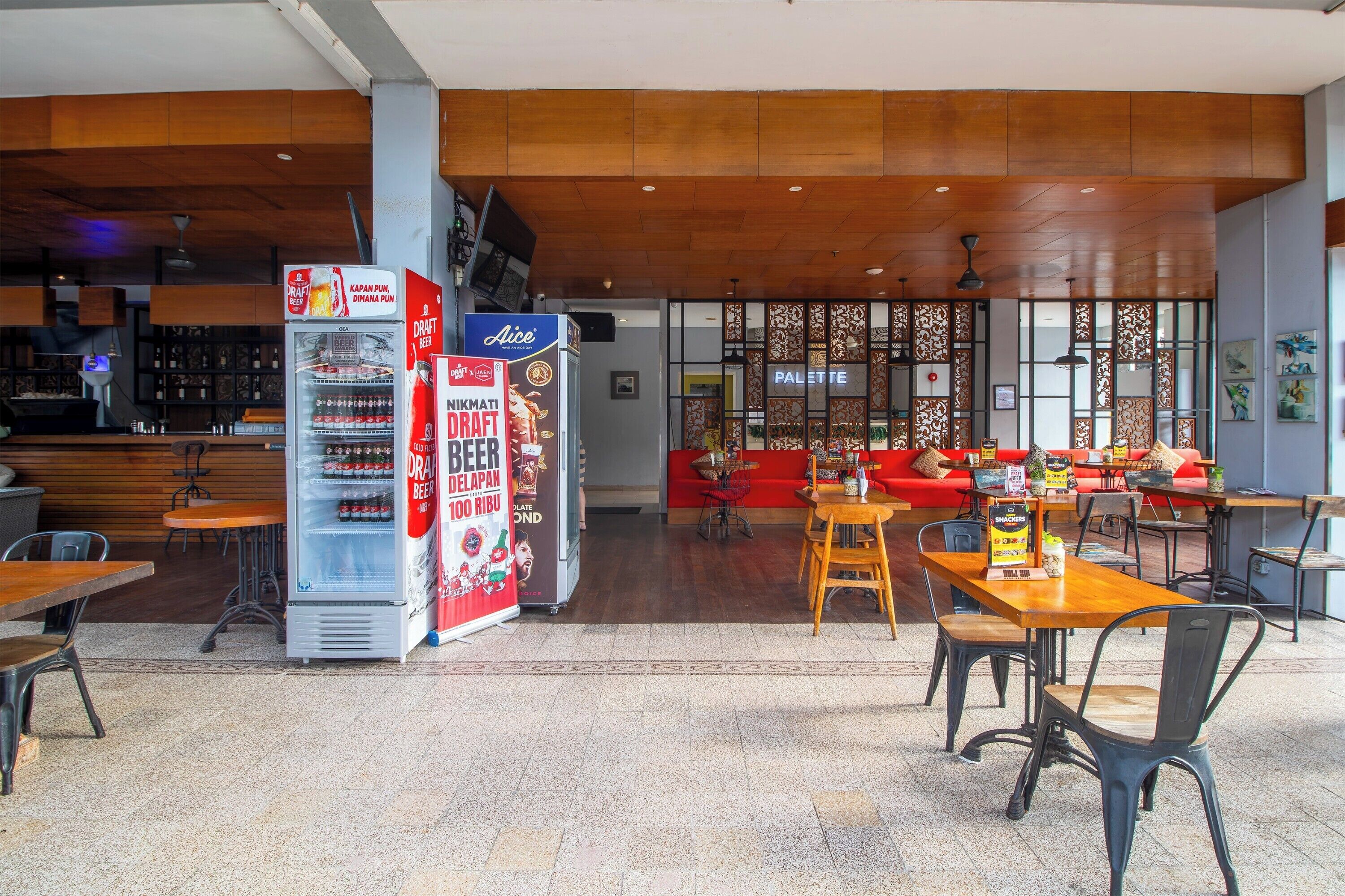 A restaurant with wooden ceiling, tables, chairs, and a refrigerator with beverage advertisements.