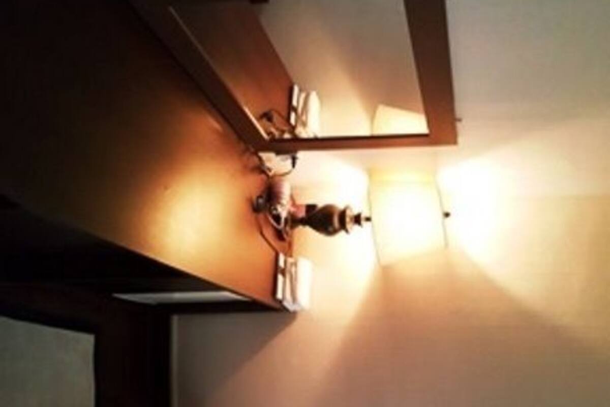 A small, dimly lit room with a single bed, a window, and a wall-mounted light fixture.
