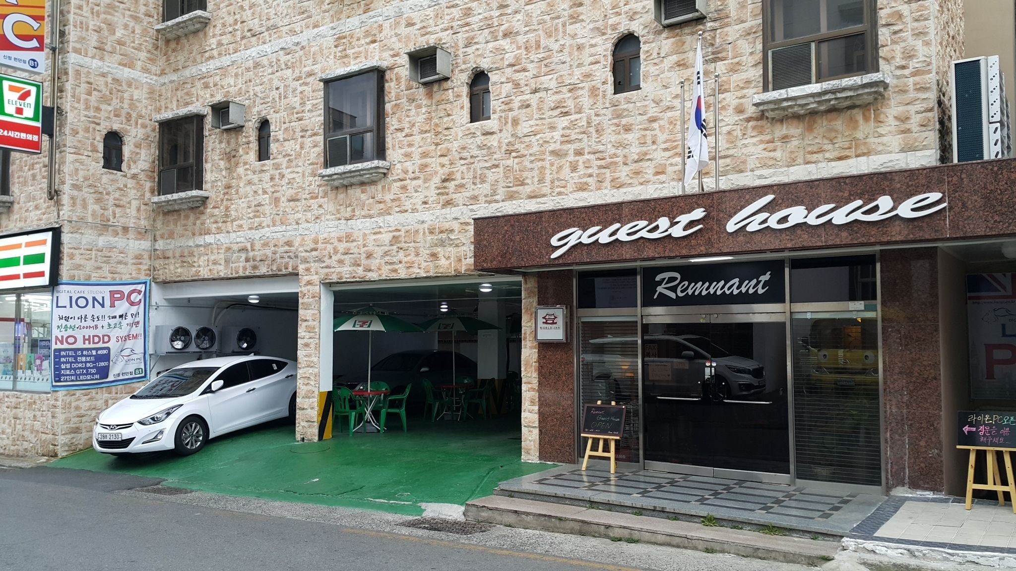 Un edificio con un cartel que dice 'guest house', una tienda 7-Eleven y un coche estacionado adelante.
