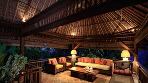 Ein Außenloungebereich mit Holzmöbeln, Fliesenboden und einem Reetdach.