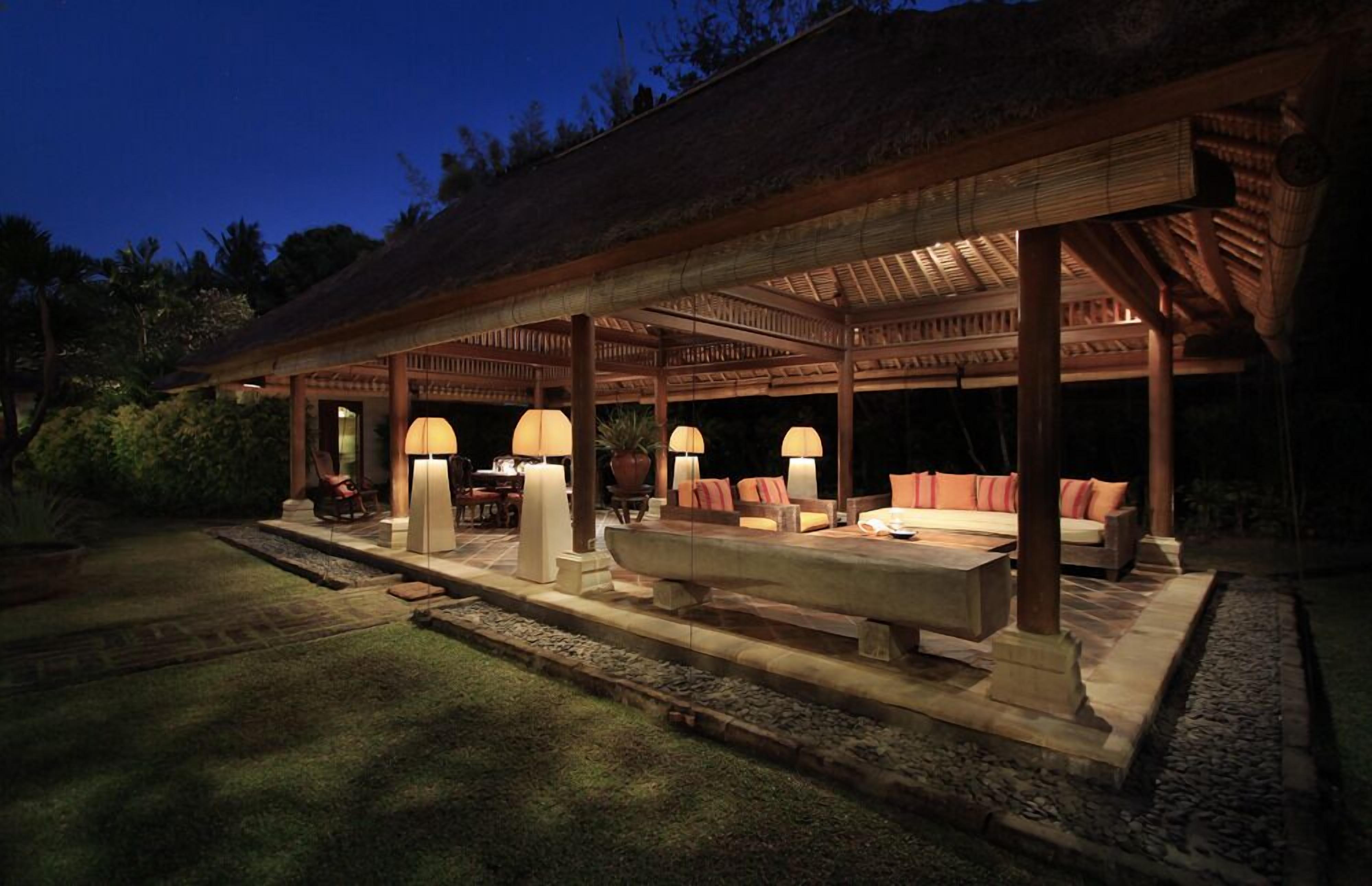 Un área de estar al aire libre techada, con mesas y sillas, rodeada por una pérgola de madera.