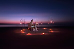 A person seated at a table with a laptop, surrounded by multiple lanterns on the ground, set against a twilight sky. - Villa Hanani (Jimbaran)