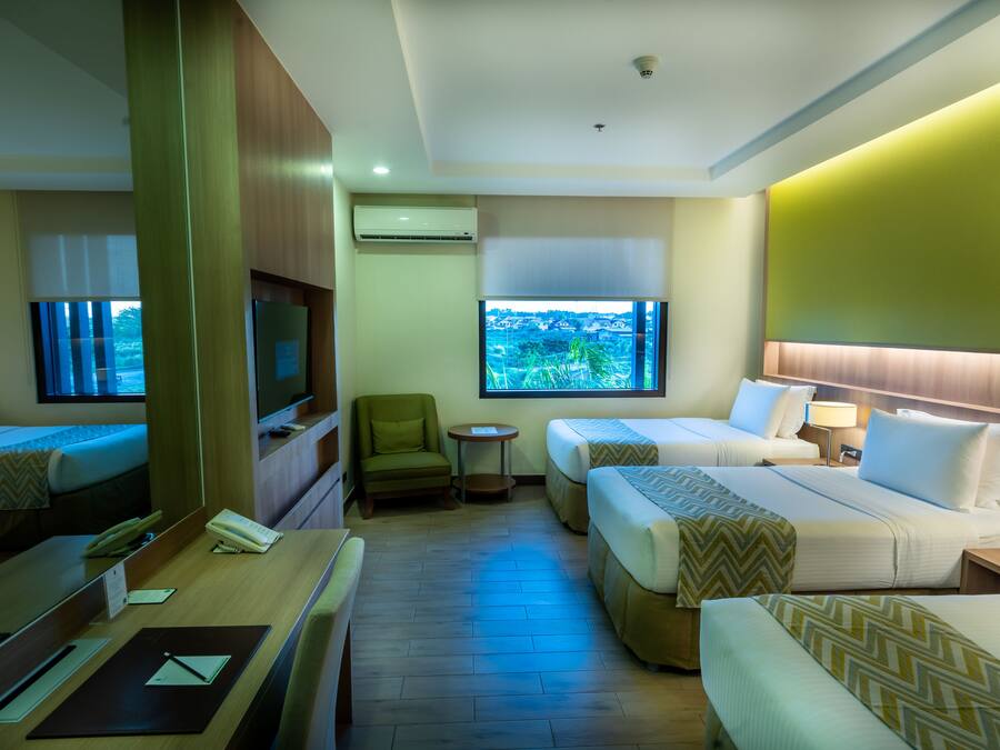A hotel room with two single beds, a desk with a chair, a small table, a TV, and a window with a view of the outdoors.