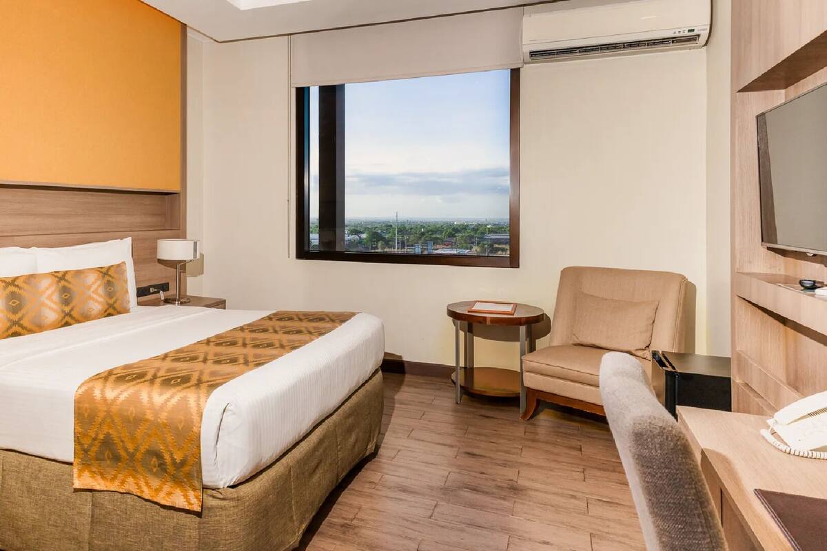 Una habitación de hotel con una cama grande, una silla, una mesita y un televisor.