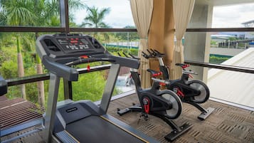 Une salle de sport équipée d’un tapis de course et de deux vélos d’appartement, avec de grandes fenêtres donnant sur un jardin.