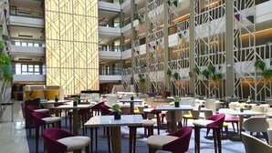 Een ruime binnenruimte met meerdere tafels en stoelen, een hoge plafond en een modern architectonisch ontwerp met geometrische patronen.