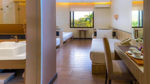 A hotel room with a large window, a bed, a desk with a chair, a sink, and a mirror.