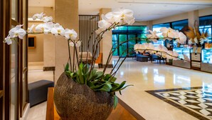 Een grote, gestructureerde vaas met witte orchideeën op een houten tafel in een hotelhal.