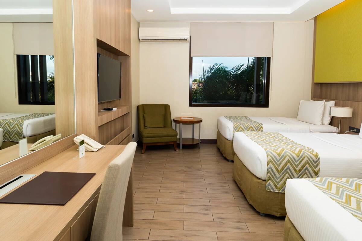 Habitación de hotel con dos camas, un escritorio, una silla, un televisor y una ventana con vistas a zonas verdes.
