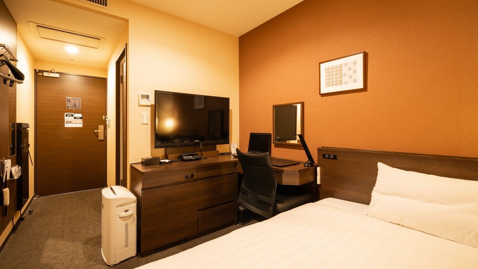 A hotel room with a bed, a desk with a computer, a television, and a minibar.