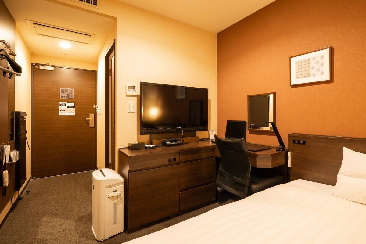 Une chambre d’hôtel équipée d’un lit, d’un bureau avec un ordinateur, d’une télévision et d’un mini-bar.