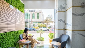 Un vestíbulo con una pared verde, una zona de estar con sillas y una mesa, y vistas a la calle con coches y un edificio que dice "Transporte".