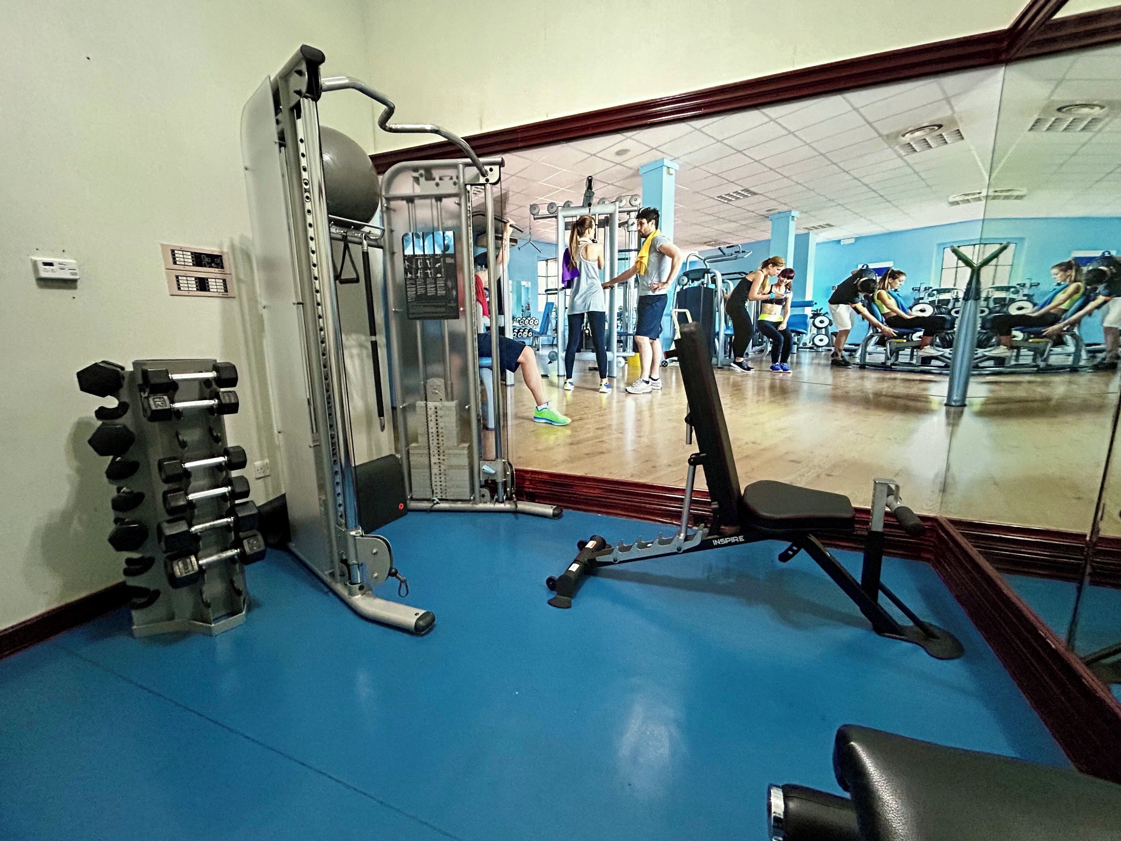 Une salle de sport équipée de matériel d’exercice, avec un miroir et un sol bleu.