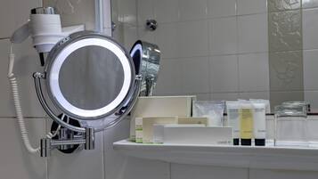 A bathroom with a hairdryer, a mirror, and a shelf with toiletries.